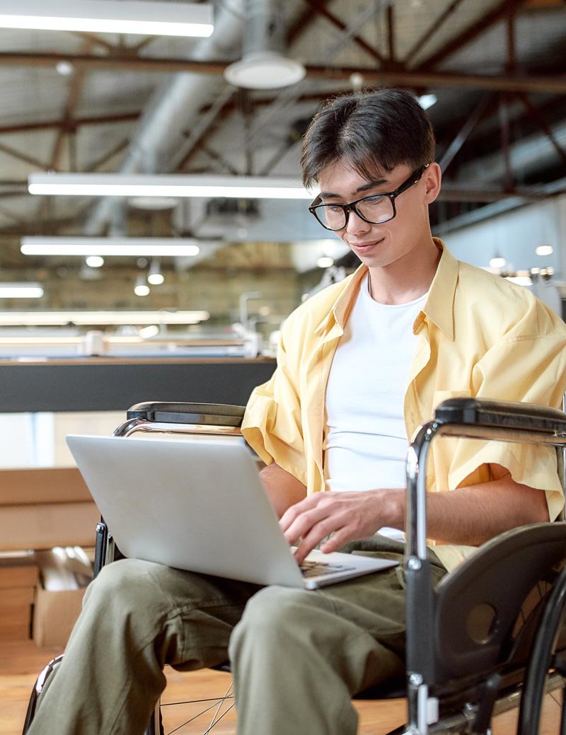 Kuva miehestä rullatuolissa kannettavalla tietokoneella työskentelemässä